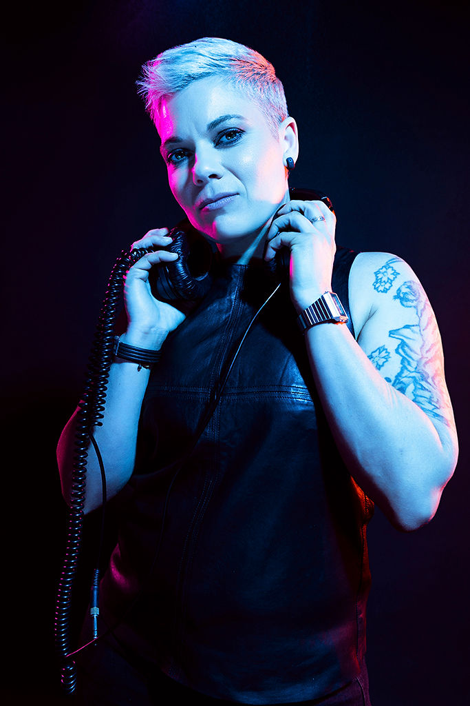 DJ Du Jour holding headphones in blue and pink studio lighting