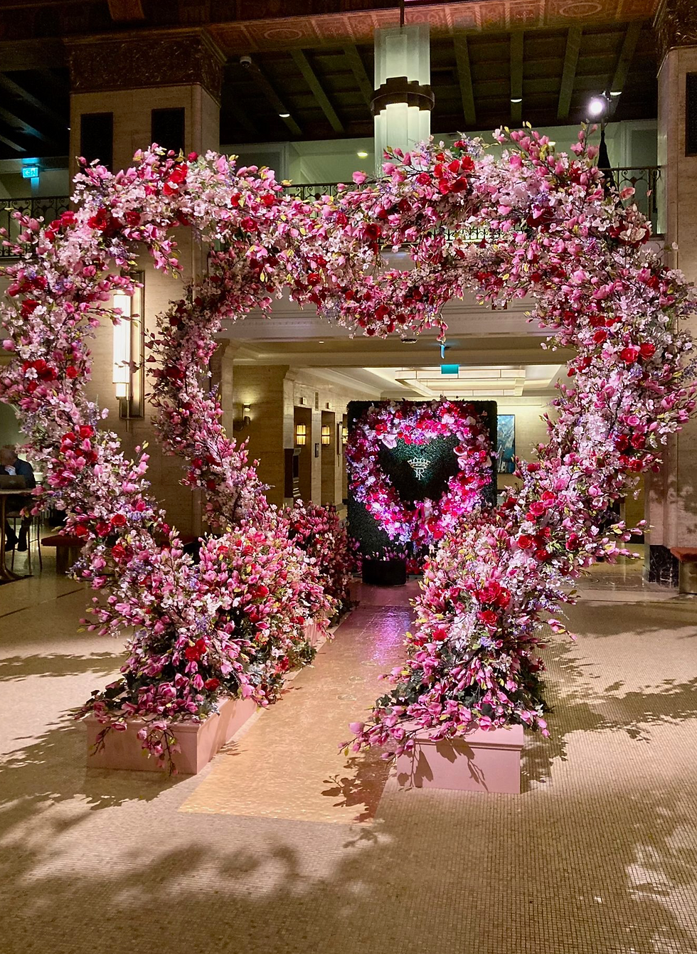 Pink and red floral heart arches stand in an elegant lobby, creating a romantic and festive atmosphere.