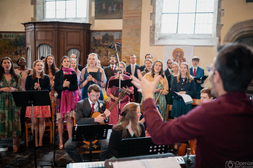 On voit une chorale avec des chanteurs et instrument et moi qui l'a dirige