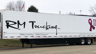 White RM Trucking trailer with 'Fight Against Cancer' ribbon