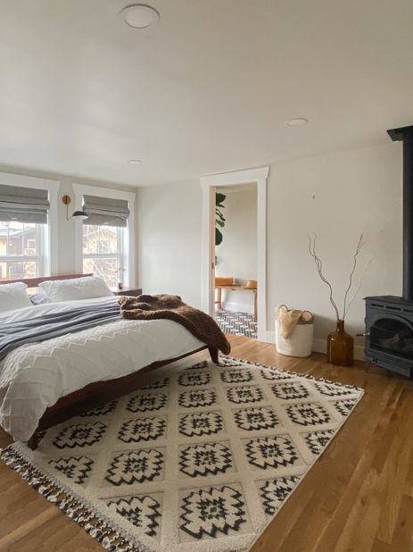 Bright bedroom with large windows, neutral bedding, and wood stove in the Berkeley neighborhood.