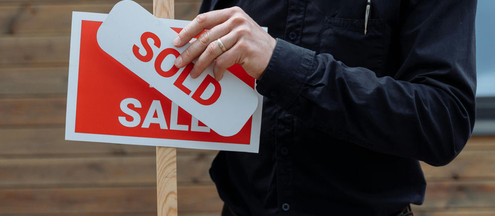 A Person Sticking a Sold Sticker on a Signboard