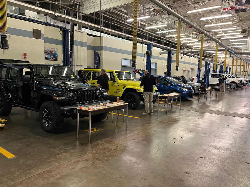A row of clean fueled vehicles parked in an automotive high bay with vendor tables in front of them on Odyssey Day.