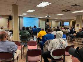 A crowd of people sitting in chairs listening to a presentation.