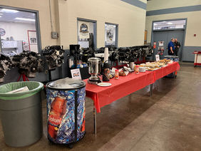 A spread of donuts and coffee on tables in an automotive high bay for Odyssey Day breakfast.