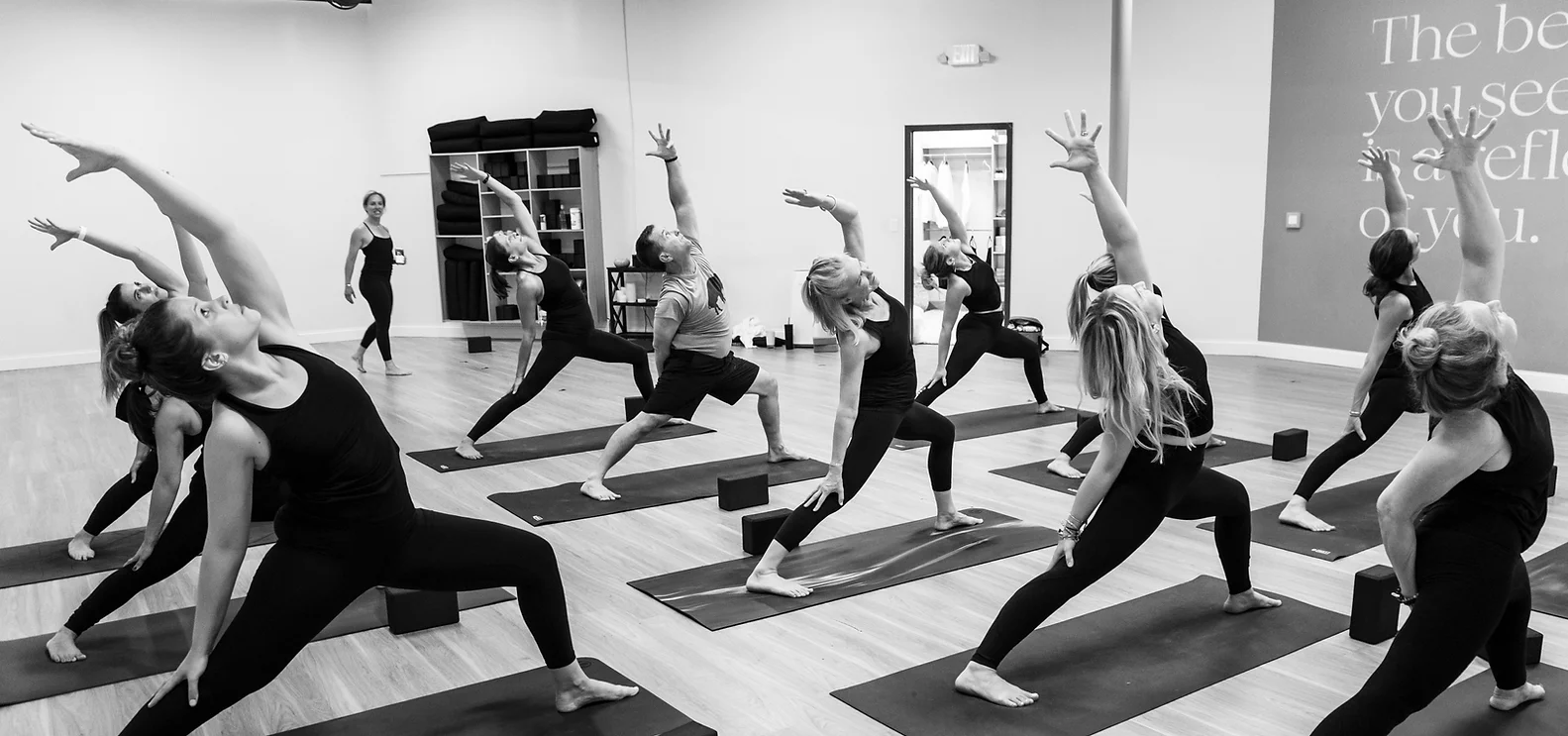 A black and white image of students in a yoga class, doing "reverse warrior" pose. Taught by Lauren Joy at The Practice Buffalo, a yoga studio.