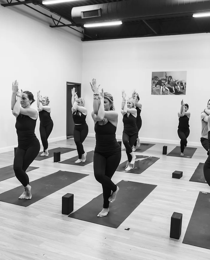 A black and white image of students in a yoga class doing Eagle Pose