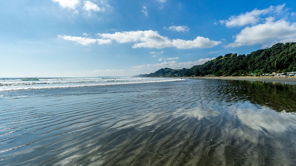 Ohope beach - Wide sandy beach with gentle waves, reflecting the blue sky and clouds, bordered by green hillside. Whakatane accountant