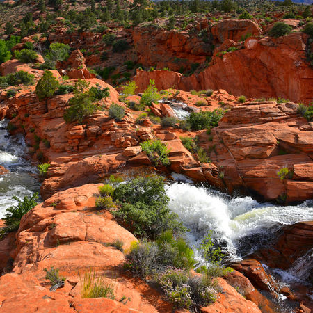 Waterfalls flowing over red sandstone cliffs at Gunlock State Park surrounded by desert landscape and blue sky