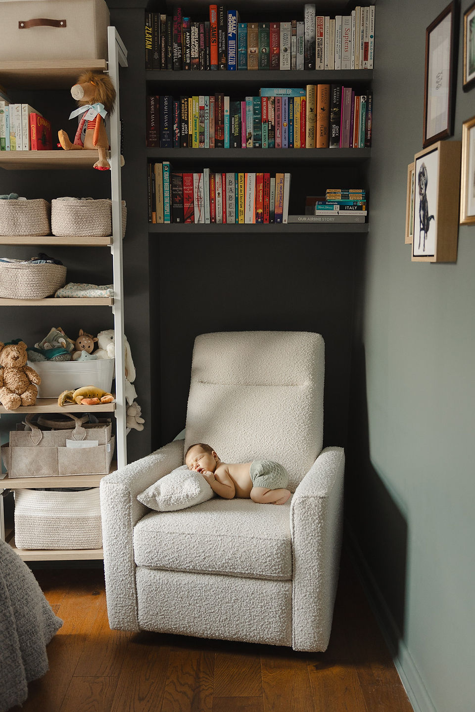 Newborn baby sleeping on cream bouclé armchair in dark green nursery during an at-home newborn photoshoot in Greenwich.