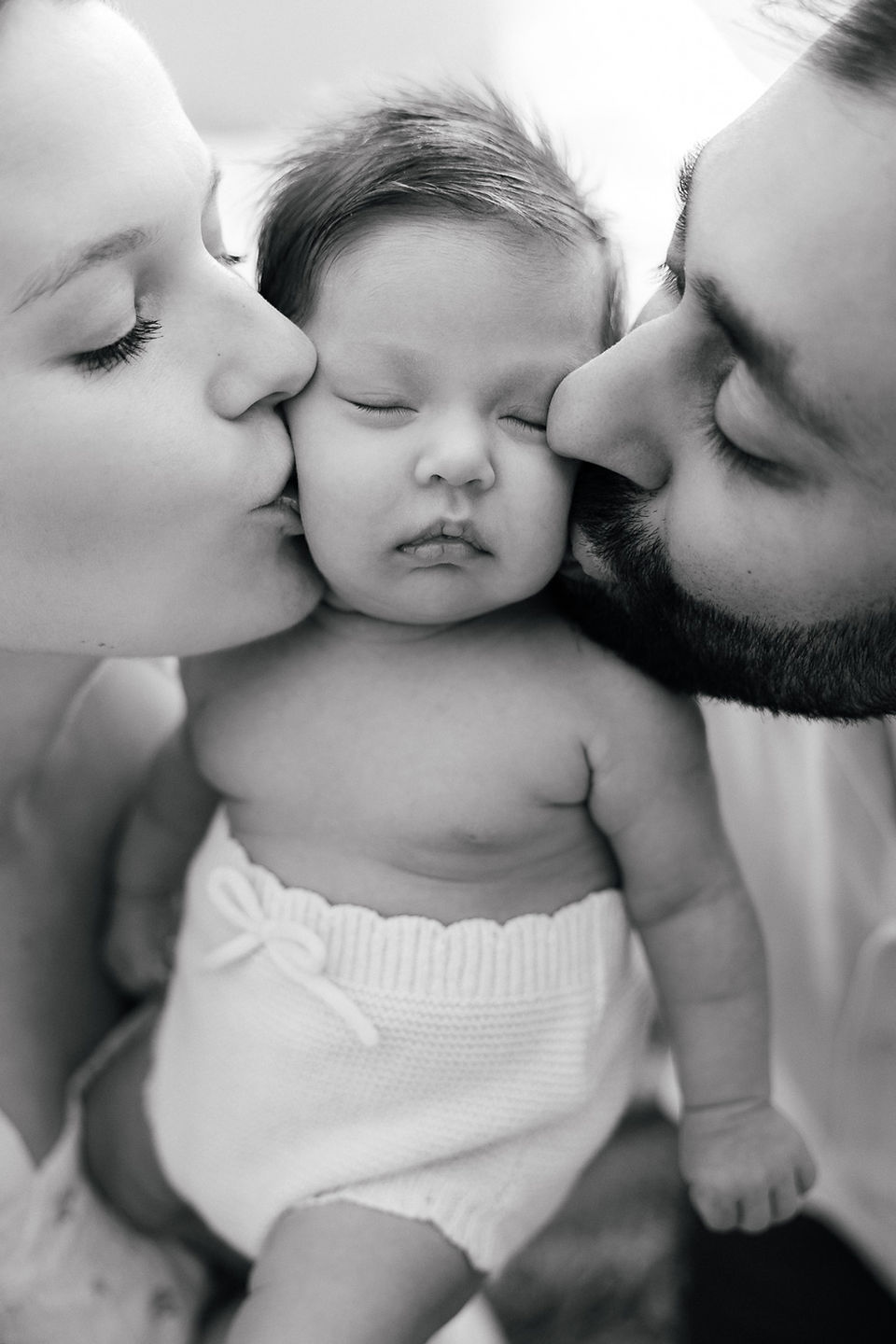 Mother and father kissing newborn baby girl on forehead during a North London in-home newborn photoshoot.