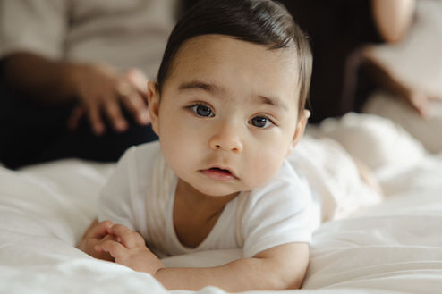 At-home baby milestone session in Wandsworth Common featuring a laughing 9-month-old sitting on a master bed