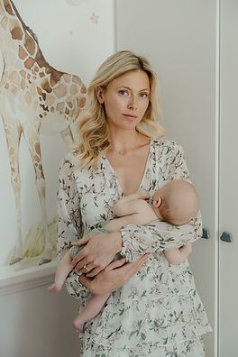A mother gently cradling her newborn baby against her shoulder in a light-filled nursery during an unposed London home photoshoot.