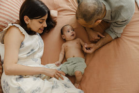 Baby lying on a bed with his parents, during an in-home newborn photography session in Holland Park, London.