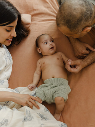 Professional baby photos London featuring new parents lying on a bed with their baby boy.