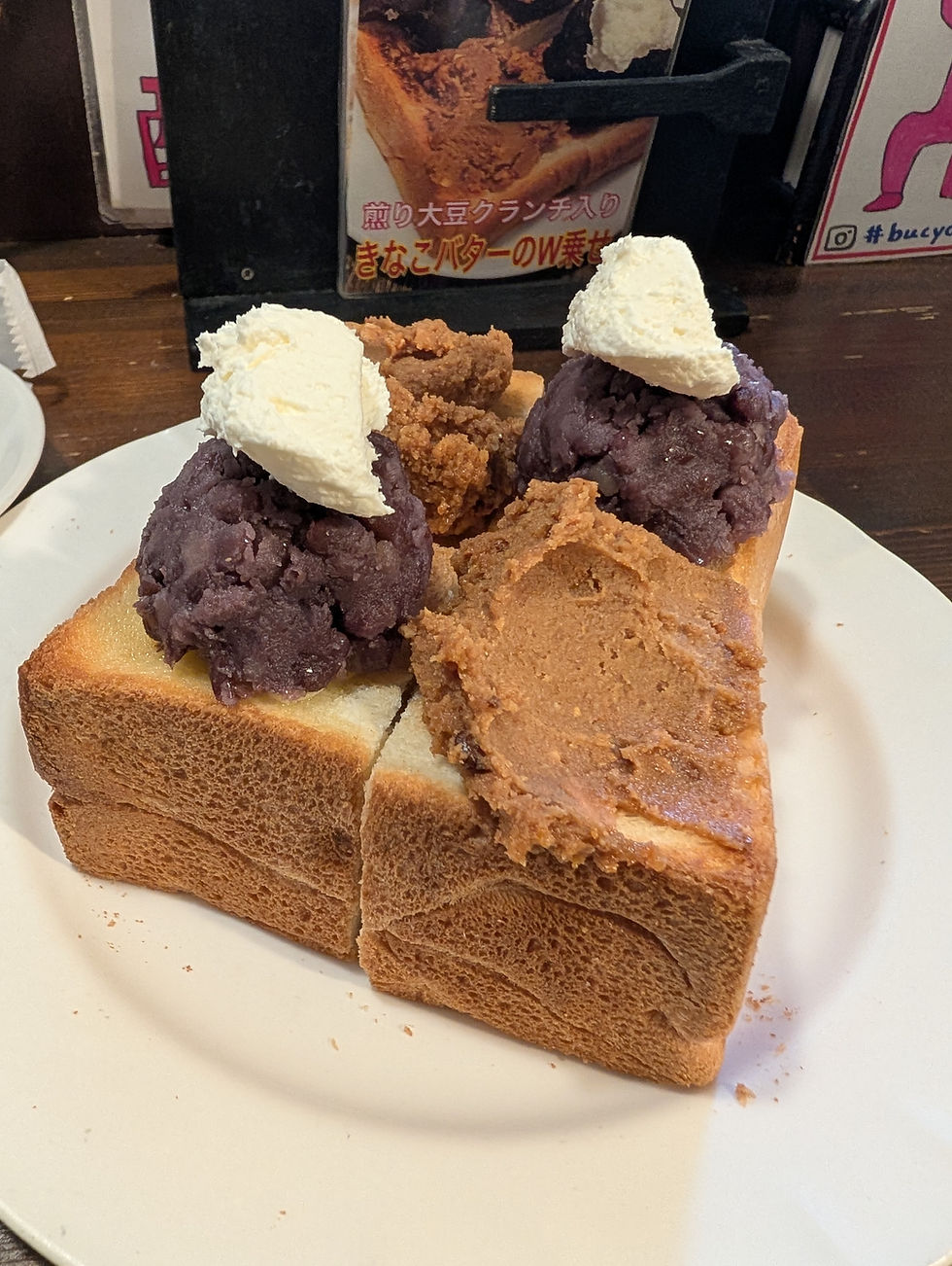 Close-up view of thick cut Ogura toast topped with kinako butter and red bean paste on a wooden plate