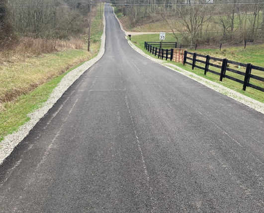 Newly paved asphalt road uphill with grass and fence