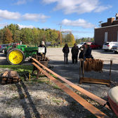 A John Deere tractor sits with people and wood frames outdoors.