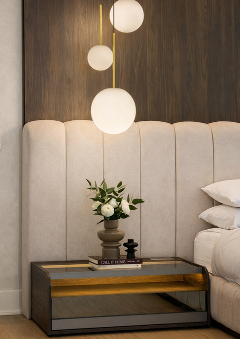 Close-up of modern nightstand, custom headboard, and sculptural pendant lighting in a serene luxury primary bedroom.