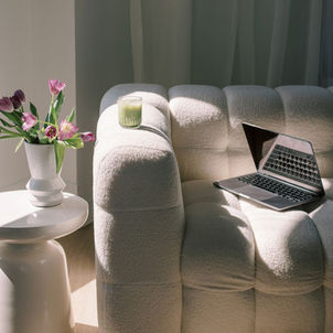 Laptop half-open on a cream sofa with a matcha drink on the arm, beside a white table with a white vase and pink flowers capturing the peaceful moment of integrating Google Analytics and Business Profile with Wix.