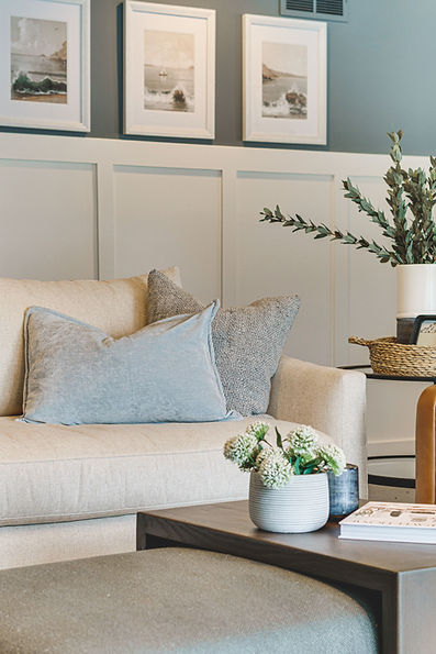 Luxury living room with beige sofa, textured pillows, wainscoting accent wall, and side table styled with a basket, plant, and decor by Design Studio Detroit.