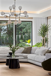 Luxury living room with white sofa, sculptural chandelier, and modern coffee tables, opening to the in-ground pool through expansive sliding doors in a contemporary Greenwich, Connecticut residence.