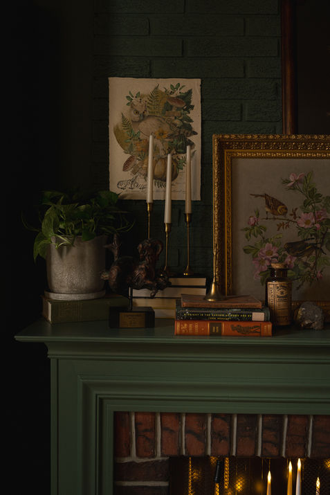 Antique fireplace with floating candles, styled objects, and nearby plant.
