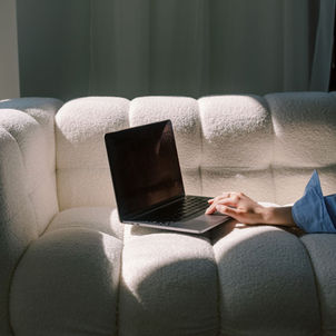 Woman’s fingers on a laptop mouse with the laptop resting on a white couch focused moment of connecting a domain to a Wix website.