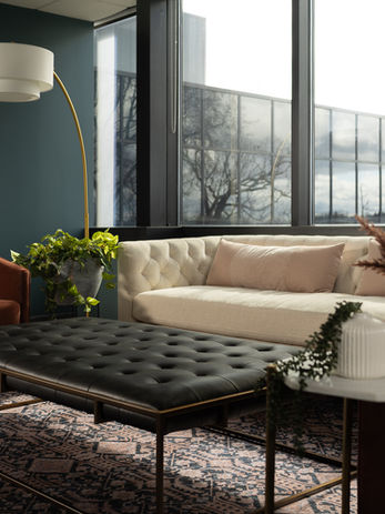 Law office interior with large picture windows, cream sofa, burgundy chairs, plants, and modern floor lamp designed by Design Studio Detroit.