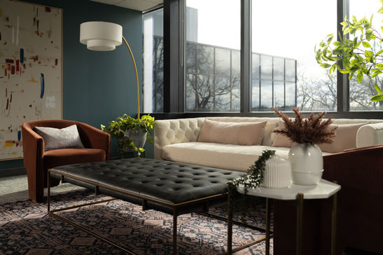 Law office interior with cream sofa, black ottoman, burgundy chairs, modern lighting, plants, and abstract artwork designed by Design Studio Detroit.