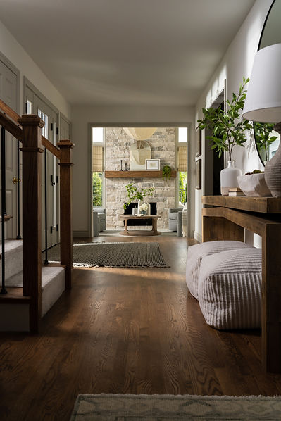 Entryway with console table and cushioned seating, rug near the front door, and a view into the living room featuring a stone fireplace with a wood beam mantle.