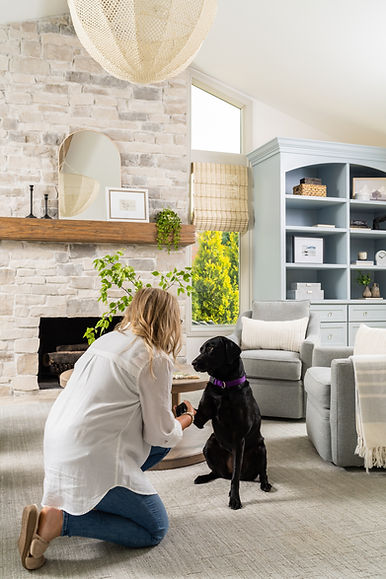 Emily Bjerke greeting the family’s black lab, Casey, in the Cobridge Project family room with stone fireplace and built-ins, showing DSD’s warm and approachable design philosophy.