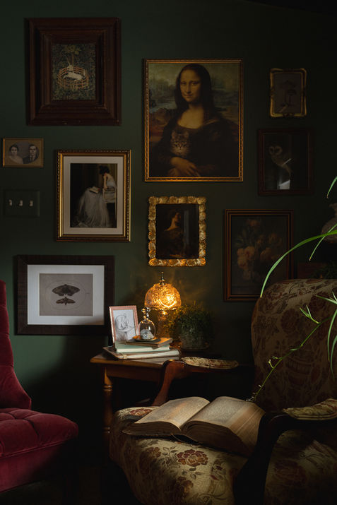 Antique floral chair with ottoman, red velvet chair, and side table with lamp and books.