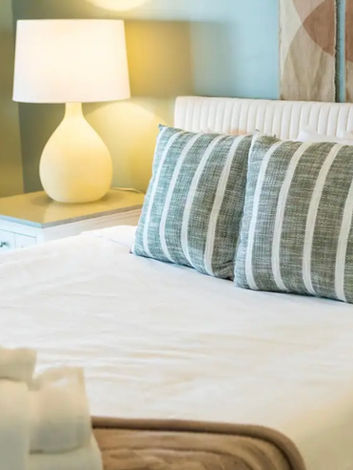 A peaceful bedroom in the Kirmar project features green walls, white bedding, and green striped accent pillows, creating a soothing atmosphere.