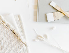 A workspace for an interior design project, featuring paintbrushes resting on a notebook, with white swatches of textured material laid out on the counter, ready for use in the design process.