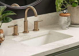 Close-up of the bathroom’s granite countertop with brass sink fixtures, green vanity, and styled details including a plant and glass containers.