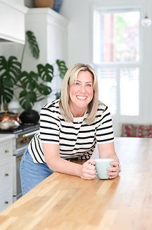 Anna Noden leaning against kitchen counter with a cup of tea and smile on her face.