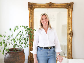 Anna smiling at camera, a plant to her left and golden antique large mirror behind her.