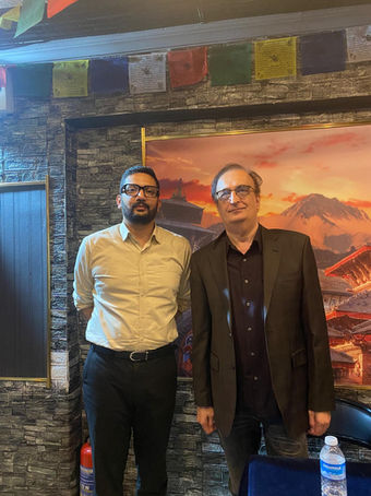 Two men by prayer flags and a landscape painting