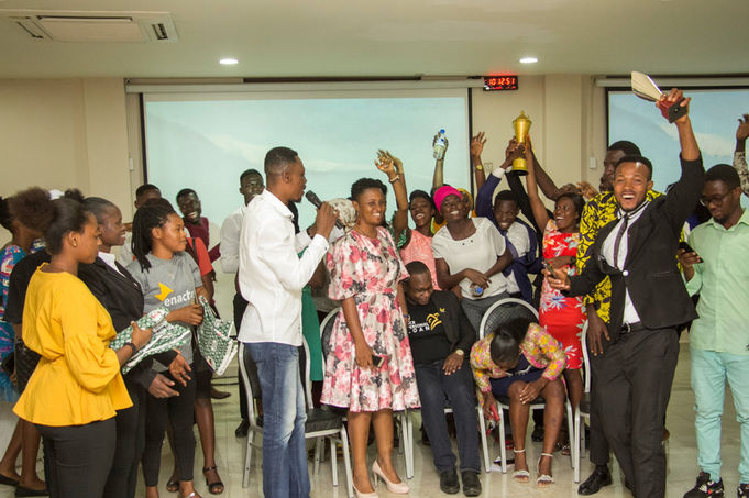 People celebrating with a trophy and a person holding a microphone