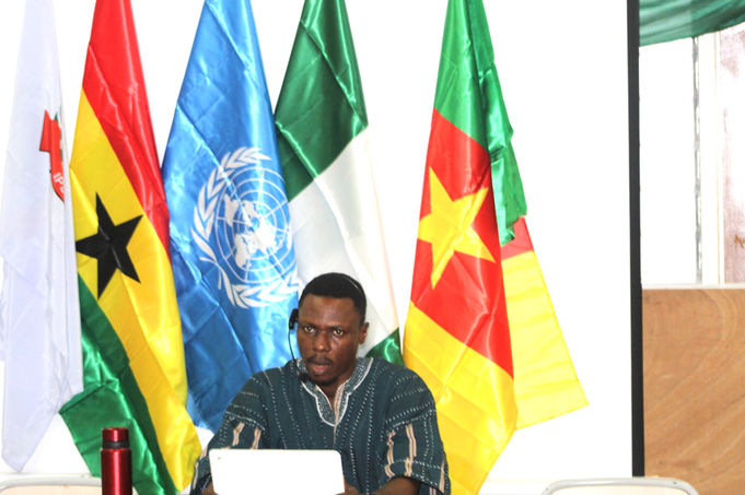 Man presenting at global peacebuilding event with UN, African flags