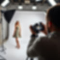 A photographer with a camera is in a photography studio, with lighting all around, taking