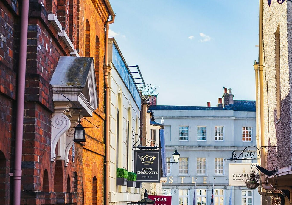 Street view with red brick buildings, signs for "Queen Charlotte" and "Clarence" against a clear blue sky, creating a quaint atmosphere.