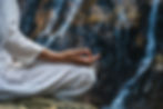Close hand of a woman in white clothes meditating on a rock by a waterfall.jpg