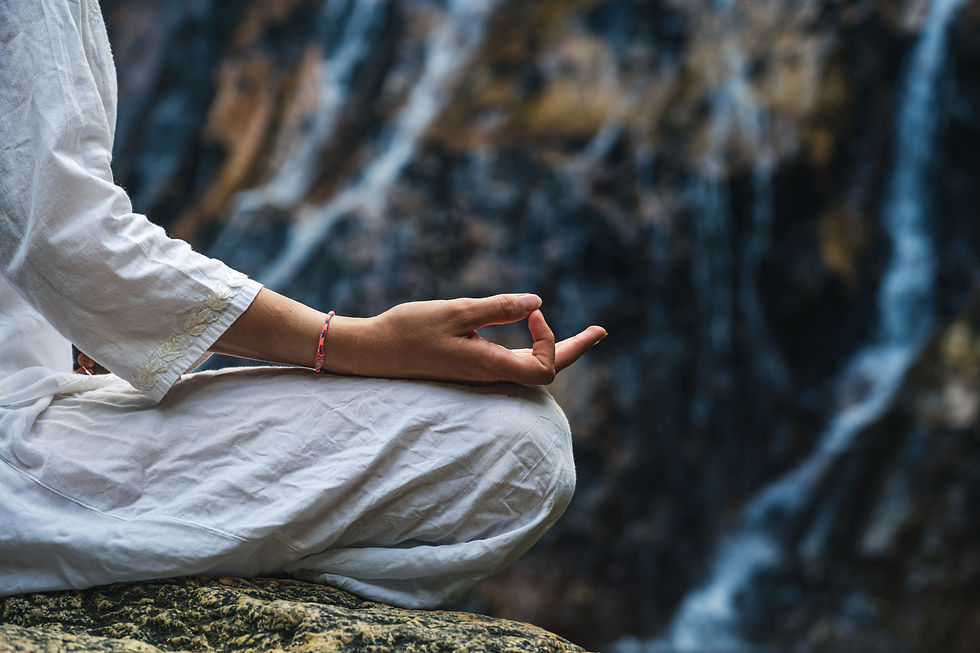 Close hand of a woman in white clothes meditating on a rock by a waterfall.jpg