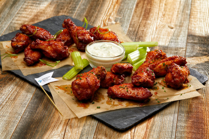 Beautifully browned chicken wings on black slate serving tray accompanied by celery and ranch dipping sauce