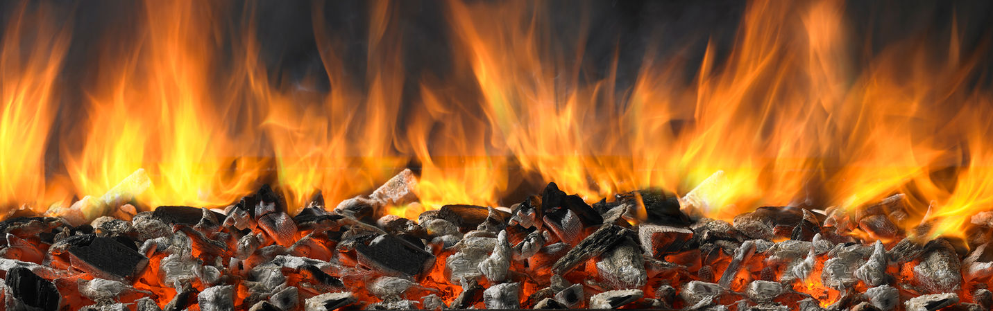 Full panoramic image of hardwood charcoal burning hot with white ash, amber glow and full flames against a dark background