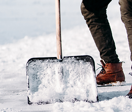 Worker using a shover to clear snow from a residential driveway.