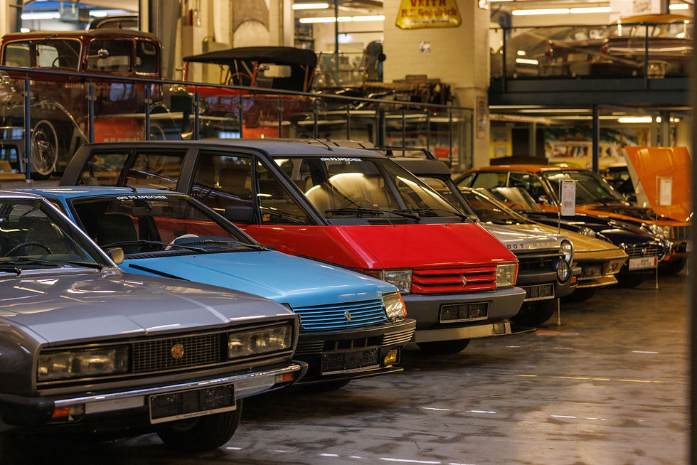 Reihe bunter Oldtimer in einer Garage. Graue, blaue und rote Wagen nebeneinander. Hintergrund zeigt Werkstattatmosphäre.