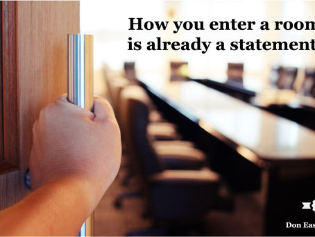 A hand grips the handle of a wooden door, pulling it open to reveal a softly blurred boardroom with a long conference table and empty chairs stretching into the background. Bold black text reads: "How you enter a room is already a statement." Don Eash Coaching logo in the lower right corner.